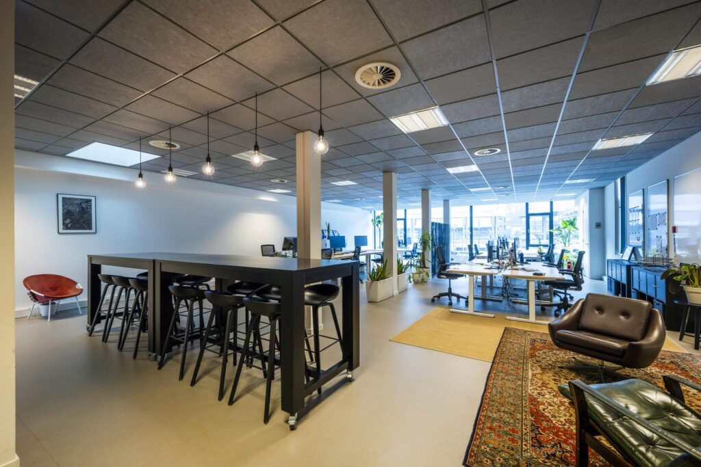 Moderne kantoorruimte aan de De Ruijterkade met open werkplekken, hoge tafels en een loungehoek.